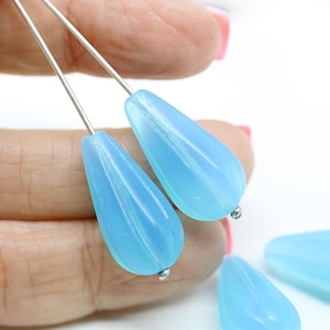 May include: Two light blue teardrop-shaped glass beads with a rippled texture, strung on silver wires.