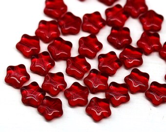 May include: A scattering of red glass star-shaped beads. The beads are translucent and have a slight shimmer.