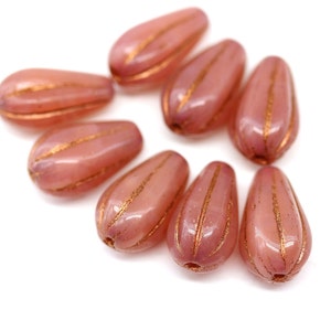 Könnte beinhalten: Eine Gruppe von acht rosa Glasperlen mit goldenen Akzenten. Die Perlen sind tropfenförmig und haben eine glänzende Oberfläche.