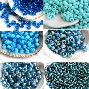 Op de afbeelding: Assortiment van blauwe glazen kralen in verschillende tinten en afwerkingen, waaronder helder, iriserend en ondoorzichtig. De kralen worden gepresenteerd in kleine witte kommen.