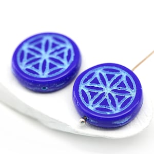 May include: Two round blue glass beads with a white geometric design. The beads are about 1 inch in diameter.