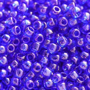 Op de afbeelding: Een close-up van een stapel iriserende blauwe kralen. De kralen zijn klein en rond, met een glanzend, reflecterend oppervlak.