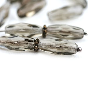 Peut inclure: Gros plan sur un brin de perles en verre gris avec des reflets argentés. Les perles sont facettées et ont un éclat métallique. Les perles sont séparées par de petites perles dorées.