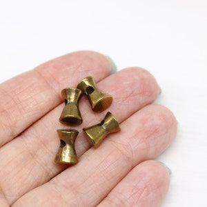May include: Four antique gold-toned metal toggle buttons with a hole in the center of each button. The buttons are in the shape of an hourglass.
