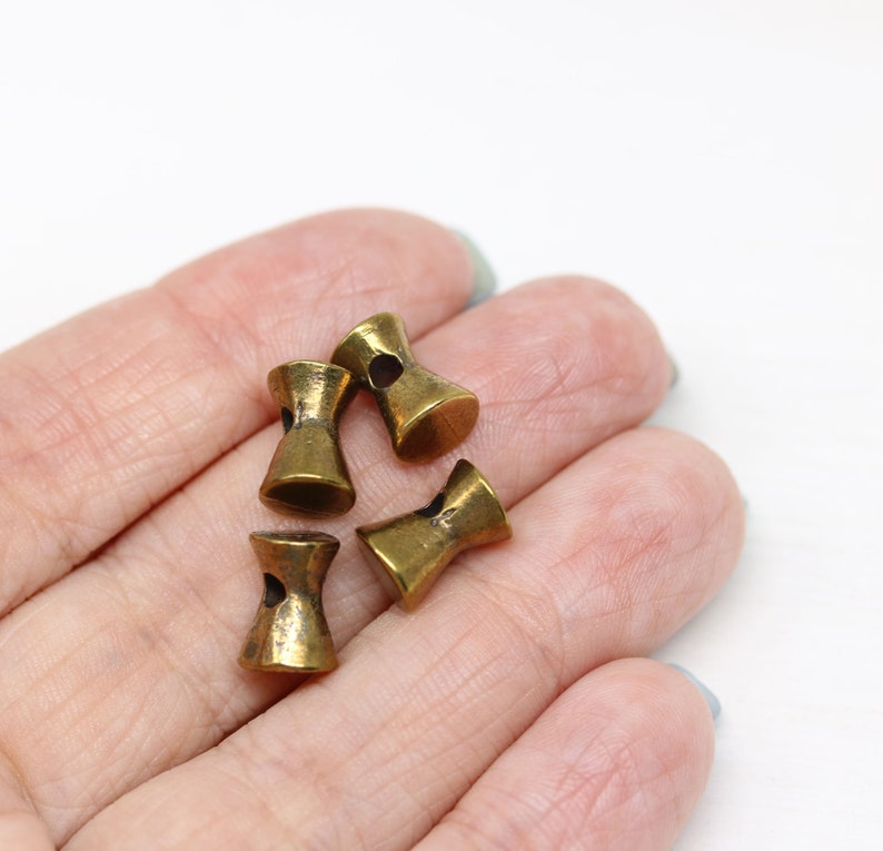 May include: Four antique gold-toned metal toggle buttons with a hole in the center of each button. The buttons are in the shape of an hourglass.