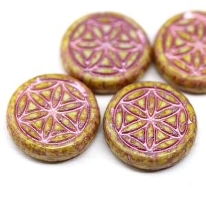 May include: Close-up of several round, yellow-brown beads with a pink geometric design. The beads have a slightly textured surface and a raised, flower-like pattern in pink. The beads are arranged on a white background.