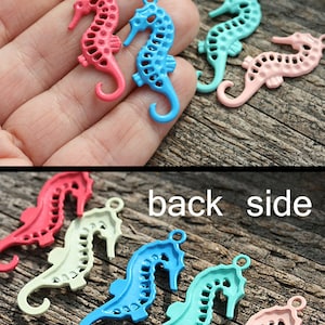May include: A set of six seahorse charms in various colors, including pink, blue, and green. The charms are made of metal and have a delicate, intricate design. The charms are shown on a wooden surface.