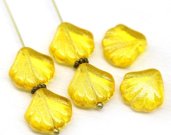 May include: Six golden yellow leaf-shaped beads with a glittery finish. Each bead is strung on a thin wire and connected with small, dark beads. The beads are arranged on a white surface.