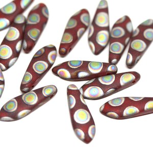 May include: A group of 15 red glass beads with iridescent silver and green accents. The beads are shaped like long, narrow ovals and have a pattern of white circles on them.
