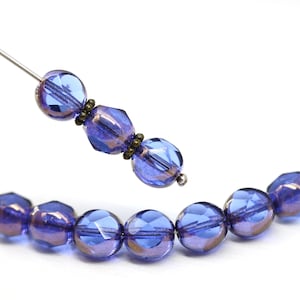 May include: Close-up of faceted blue glass beads with a metallic sheen. The beads are strung on a silver wire, with a few beads separated from the main strand. The beads have a round and geometric shape.