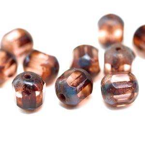 May include: A group of brown and blue glass beads with a faceted design. The beads are scattered on a white surface.