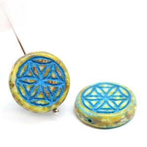 May include: Two round, yellow and blue ceramic beads with a carved flower of life design.