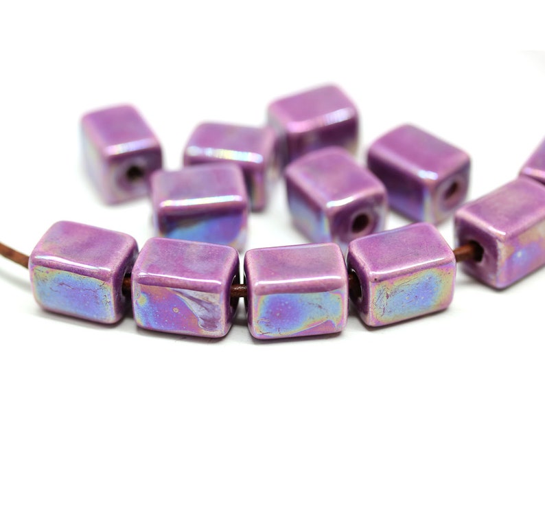 May include: A strand of iridescent purple ceramic square beads. The beads have a glossy finish and are strung on a brown cord.