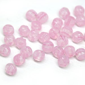 Peut inclure: Un ensemble de perles roses translucides avec un motif ray&eacute;. Les perles sont rondes, certaines ayant une forme florale. Elles sont dispos&eacute;es sur une surface blanche, cr&eacute;ant une esth&eacute;tique d&eacute;licate et f&eacute;minine. Id&eacute;al pour la cr&eacute;ation de bijoux.