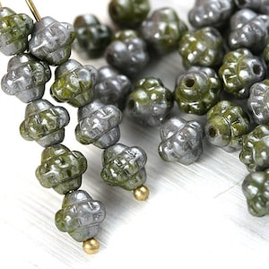 Könnte beinhalten: Eine Strähne aus grünen und silbernen Glasperlen mit einem blumenartigen Design. Die Perlen sind auf einem Draht aufgefädelt und haben eine metallische Oberfläche.