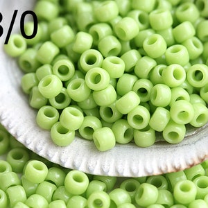 May include: A close-up of a bowl filled with light green glass beads. The beads are round and have a hole in the center. The text "8/0" is visible in the top left corner of the image.