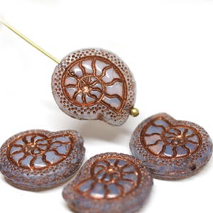 Peut inclure: Quatre perles en verre de couleur lilas clair avec un motif d'ammonite de couleur cuivre. Les perles sont de forme irrégulière et ont une surface texturée.