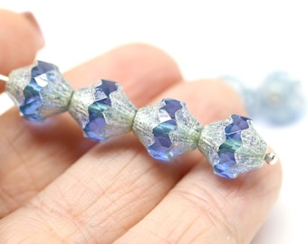 Può includere: Una fila di perline di vetro iridescente blu e argento. Le perline sono sfaccettate e hanno una superficie ondulata e testurizzata.