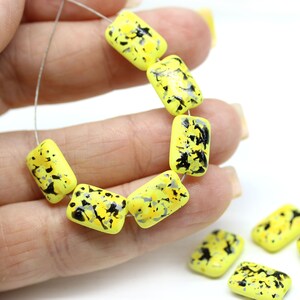 May include: A strand of yellow and black rectangular glass beads with a speckled pattern. The beads are strung on a silver wire.