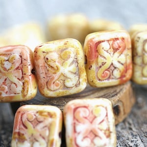 Könnte beinhalten: Nahaufnahme einer Kette aus quadratischen Perlen mit einem geschnitzten Design. Die Perlen sind cremeweiß mit einem hellorangen und rosafarbenen Überzug.