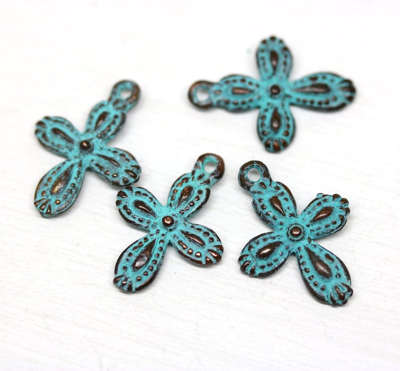 May include: Four turquoise blue metal flower charms with a distressed finish. Each charm has a loop for attaching to jewelry or other crafts.