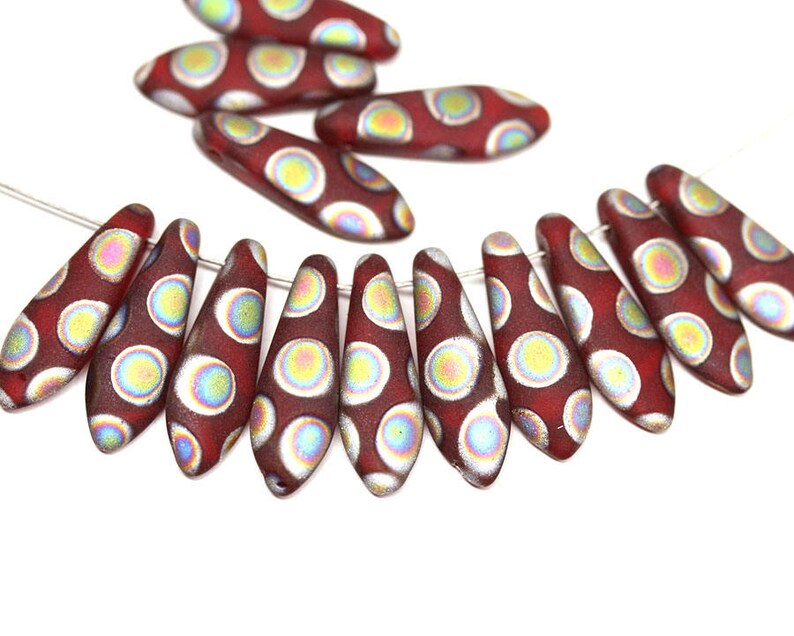 May include: A strand of red glass beads with iridescent white polka dots. The beads are shaped like teardrops and are strung on a silver wire.