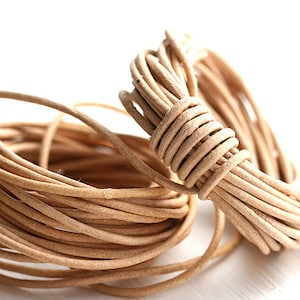 May include: A close-up of a coil of natural-colored leather cord. The cord is soft and supple, and it is perfect for crafting jewelry, accessories, and other projects.