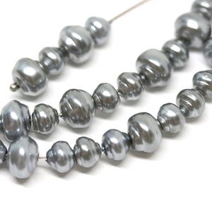 Puede incluir: Una hebra de perlas barrocas de color plateado. Las perlas son de forma irregular y tienen un acabado liso y brillante.