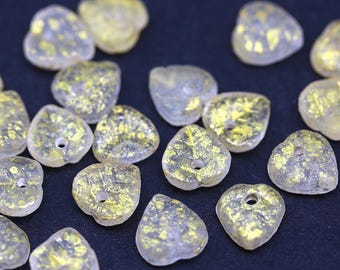 May include: A collection of heart-shaped beads. The translucent beads have a gold leaf design and a small hole for stringing. The beads are scattered on a dark surface.