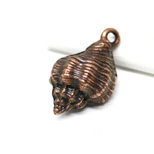 May include: A copper-coloured seashell charm with a loop for hanging. The seashell has a detailed, textured surface.