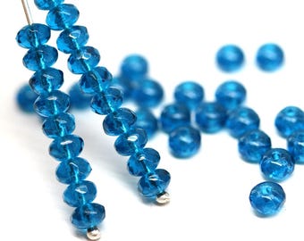 May include: Close-up of several strands of faceted, transparent, turquoise-blue beads. The beads are strung on thin silver wires, with some loose beads scattered around. The beads have a sparkling, crystal-like appearance.