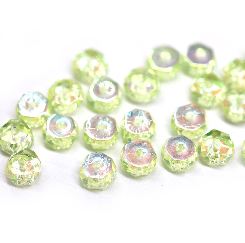 May include: A scattering of iridescent green glass beads, each with a faceted hexagonal shape and a hole in the center.