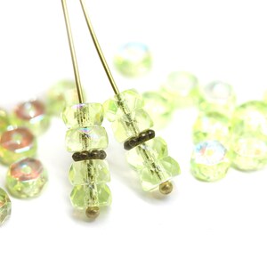 May include: Two strands of green glass beads with gold accents on a white background. The beads are faceted and have a slight iridescent sheen.