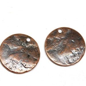 May include: Two round copper metal charms with a hammered texture and a hole for hanging. The charms are a mix of copper and silver tones.