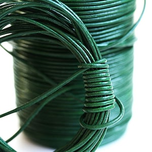 May include: A spool of dark green leather cord. The cord is wound tightly around the spool and is ready to be used for crafting projects.