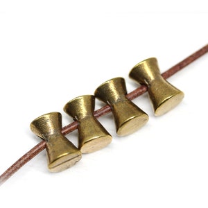 May include: Five gold-colored metal beads with a flared design, strung on a brown leather cord.