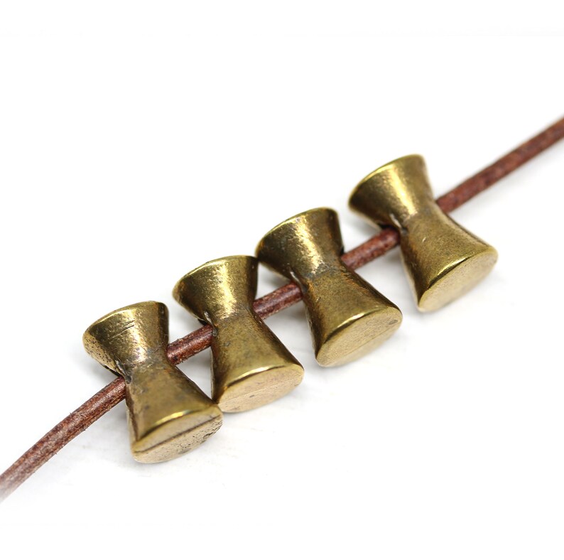 May include: Five gold-colored metal beads with a flared design, strung on a brown leather cord.