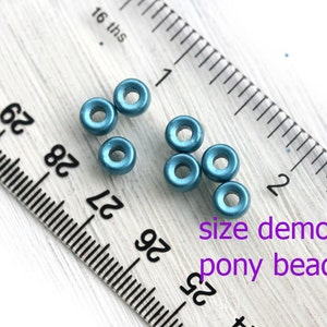 May include: Close-up of teal blue pony beads next to a ruler. The beads are about 1/4 inch in diameter. "size demo pony beads" is written in purple text below the beads.