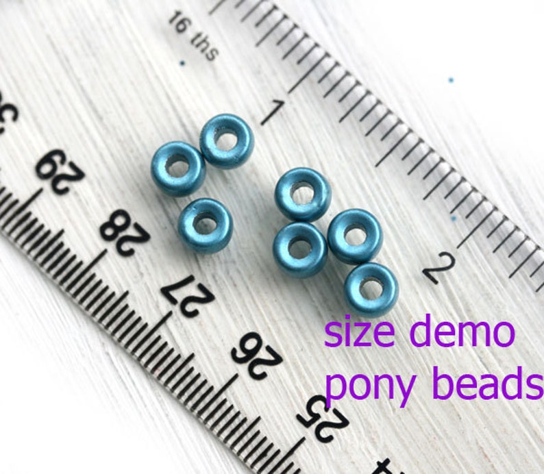 May include: Close-up of teal blue pony beads next to a ruler. The beads are about 1/4 inch in diameter. "size demo pony beads" is written in purple text below the beads.
