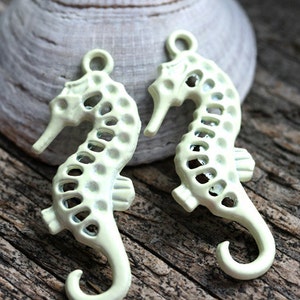 May include: Two pale yellow metal seahorse charms with a cutout design. The charms have a loop at the top for attaching to jewelry or other crafts.