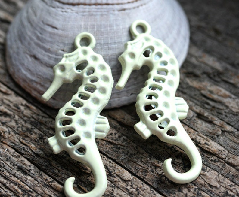 May include: Two pale yellow metal seahorse charms with a cutout design. The charms have a loop at the top for attaching to jewelry or other crafts.