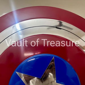 May include: A close-up of a shield with a red, white, and blue color scheme. The shield has a silver border and a blue star in the center. The text "Vault of Treasure" is visible.