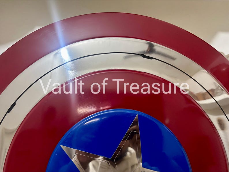 May include: A close-up of a shield with a red, white, and blue color scheme. The shield has a silver border and a blue star in the center. The text "Vault of Treasure" is visible.