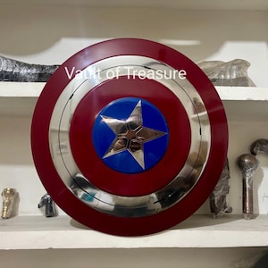 May include: A Captain America shield replica. The shield features a red outer ring, a silver inner ring, and a blue center with a silver star. The text "Vault of Treasure" is visible on the shield.