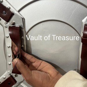 May include: A silver-colored shield with brown leather straps and metal rivets. The text "Vault of Treasure" is visible on the shield's surface. The shield has a circular design.