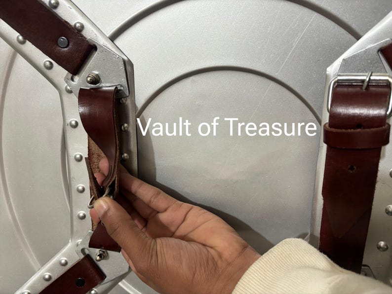 May include: A silver-colored shield with brown leather straps and metal rivets. The text "Vault of Treasure" is visible on the shield's surface. The shield has a circular design.