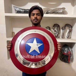 Può includere: Uno scudo di Captain America con una combinazione di colori rosso, bianco e blu. Lo scudo presenta una stella bianca su un cerchio blu, circondata da un anello argentato e un anello esterno rosso. Il testo "Vault of Treasure" è visibile.