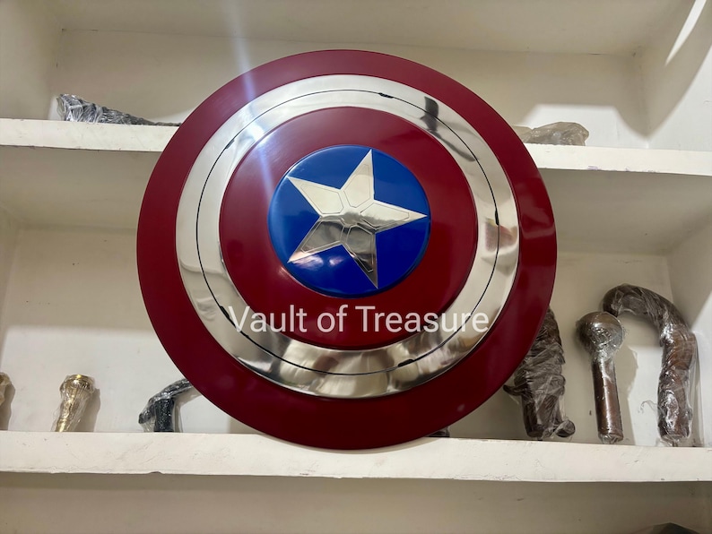 May include: A Captain America shield replica. The shield is primarily red with a silver metallic ring and a blue center featuring a white star. The text "Vault of Treasure" is visible on the shield.