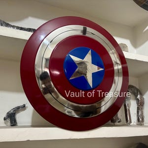 May include: A red, silver, and blue shield with a star emblem. The shield has a circular design with a red outer ring, a silver middle ring, and a blue center with a white star. The text "Vault of Treasure" is visible.