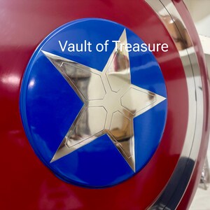 May include: A red, white, and blue shield with a large silver star in the center. The star is set against a blue circle, and the shield has a metallic silver border. The text "Vault of Treasure" is visible on the blue circle.